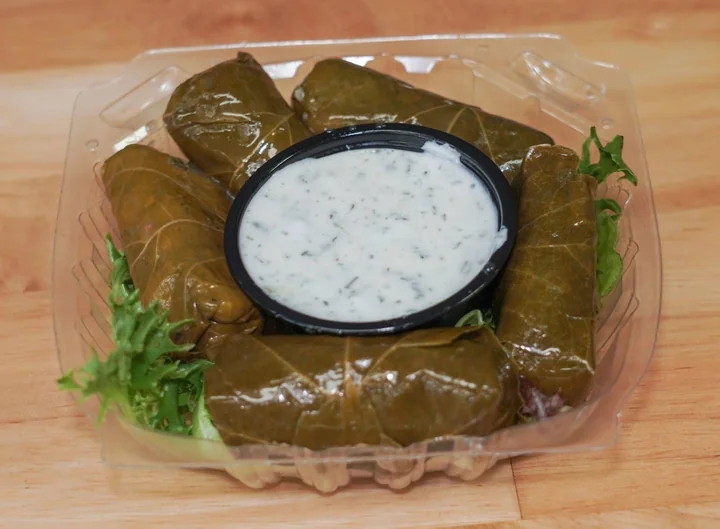 Stuffed grape leaves arranged around a cup of tzatziki.
