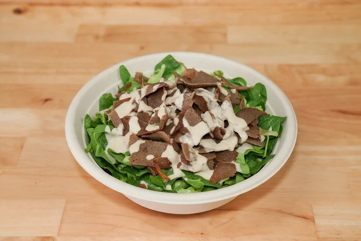 Lamb gyro meat over fresh greens with tahini.