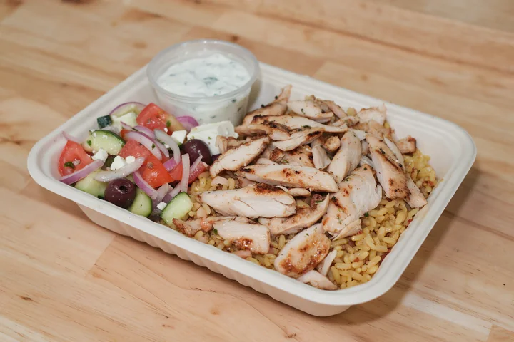 Chicken shawarma over seasoned rice with Greek salad and sauce.