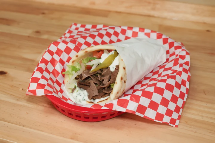 Sliced lamb gyro with vegetables and tzatziki in pita.