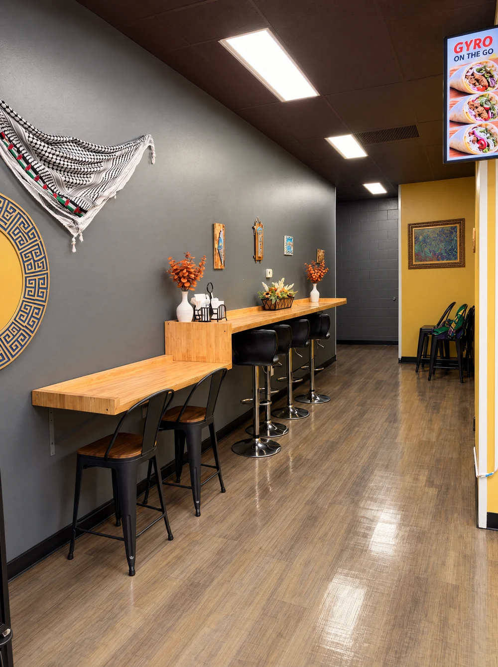 Inside Gyro on the Go: wood tables, counter seating and a Palestinian keffiyeh displayed on the wall.